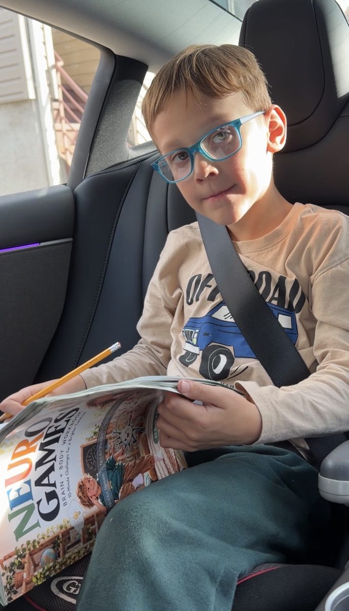 A boy holds Neuro Games in the back seat of a car